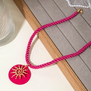 Detail of rose pink rope necklace with gold sun pendant on a velvet jewelry tray