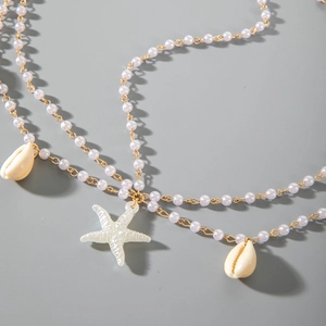 Détail de chaîne dorée bohème avec perles blanches, étoile de mer et coquillages