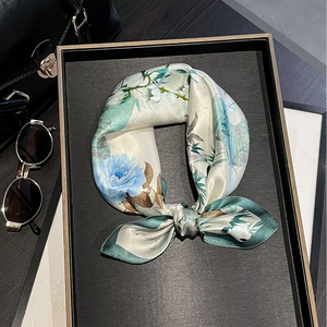 Silk scarf with blue rose pattern tied in a bow on a black wooden tray with sunglasses