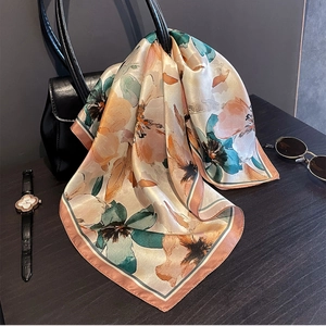 Silk square scarf with floral print tied to a leather handbag in a lifestyle setting