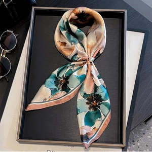Detail of silk floral scarf with elegant pearl brooch on leather tray and sunglasses