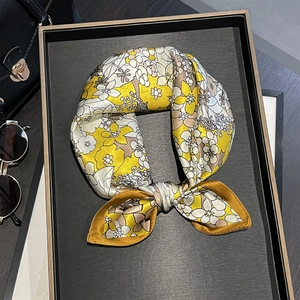 Detail of floral silk scarf tied in a bow on a black tray with stylish accessories