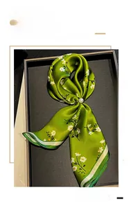 Dettaglio della sciarpa in seta verde con fiori e chiusura con perla bianca