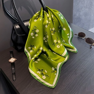 Foulard in seta verde a fiori annodato a una borsa a mano in pelle nera elegante