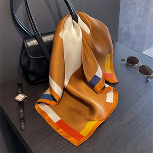 Dettaglio di un foulard di seta stampato con motivi geometrici legato a una borsa di pelle