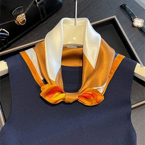 Dettaglio di un foulard di seta annodato a fiocco su un gilet in maglia blu navy