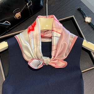 Elegant silk scarf with pink and white print tied on a dark blue knit top for women