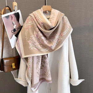Detailed close-up of floral jacquard scarf with fringe edges on a white coat