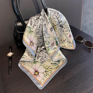 Close-up of floral silk square scarf elegantly tied on a black leather designer handbag