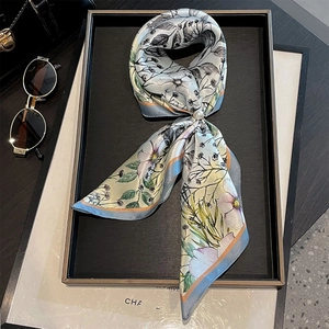 Close-up of a floral silk twilly scarf in blue and beige with a pearl accessory and sunglasses