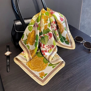 Elegant silk scarf with yellow rose print draped over a black leather handbag