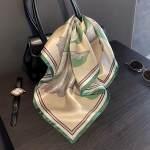 Detail of vintage mulberry silk scarf with green floral print tied to a black leather bag