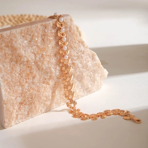 Detailaufnahme des goldenen Blattarmbands mit kleinen weißen Perlen auf Naturstein