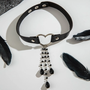 Choker gotico in pelle nera con anello a cuore argento e catenelle su sfondo bianco puro