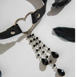 Dettaglio choker punk gotico con cinturino in pelle nera, cuore d'argento e perline