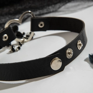 Dettaglio macro del girocollo punk in pelle con anello a cuore argento e pendente