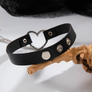 Dettaglio choker in pelle gotica con anello a cuore argento e catene drappeggiate su legno