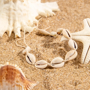 Bohemian cowrie shell anklet with woven cord on beach sand with sea shells