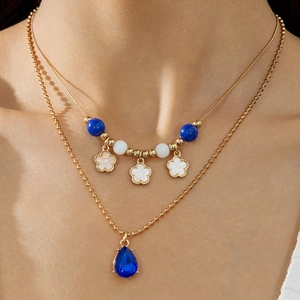 Details einer mehrlagigen Goldkette mit blauem Tropfenanhänger und Blumenanhängern