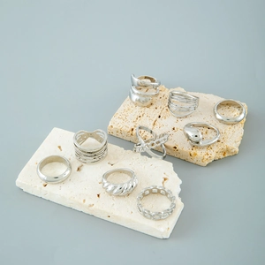 Set of 8 silver punk-style geometric rings displayed on artistic beige travertine stone