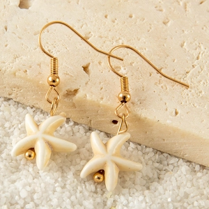 Bohemian gold starfish earrings with white shell texture on beach stones and sand