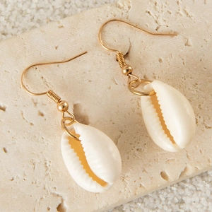 Detail of bohemian shell drop earrings with gold hooks on a textured marble background