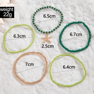 Detail of 5-piece green beaded anklet set with starfish charm on beach sand texture