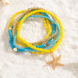 Close-up of Bohemian beaded anklets with starfish charms on white beach sand