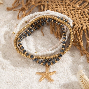 Close-up of bohemian beaded anklet set with a textured gold starfish charm on white sand