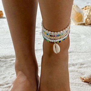 Close-up of bohemian layered anklet with colorful beads and natural shell on sand