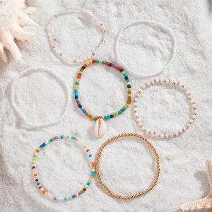 Detail of bohemian starfish shell anklet set with colorful beads on white beach sand