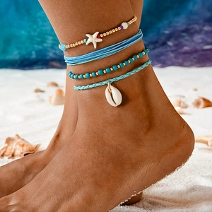 Bohemian multilayer shell and starfish anklet set worn on a sandy beach at the ocean