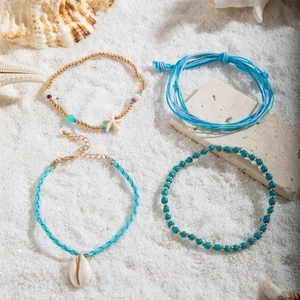Detail of bohemian shell and starfish beaded anklet set on a white sand beach background