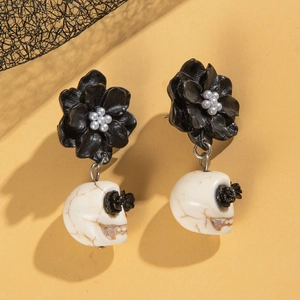 Detail of gothic earrings featuring black petals, white skulls, and dark rose eyes