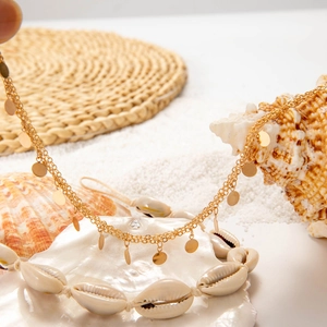 Detail of beach jewelry set featuring a cowrie shell necklace and gold sequin chain