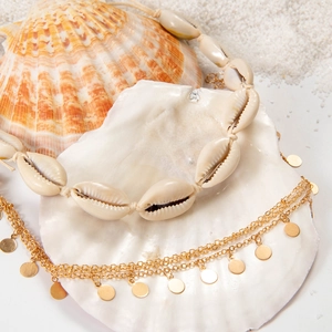 Detailed view of bohemian cowrie shell necklace and gold layered chain on white sand