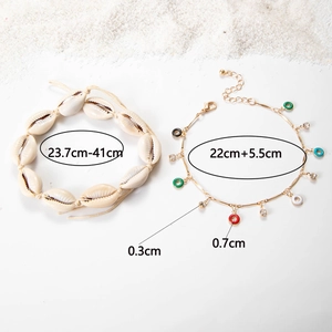Detail view of Bohemian shell anklet and gold chain with colorful enamel charms on sand