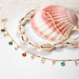 Detail of bohemian shell necklace and colorful beaded anklets on white sand beach background