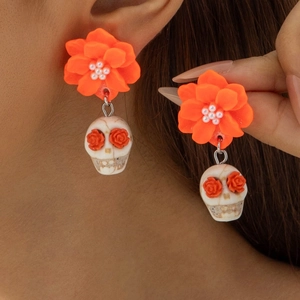 Close-up of Halloween skull earrings with orange flowers and pearl accents worn by a model