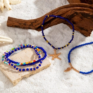 Detail of bohemian beach anklets with starfish and feather charms on white sand
