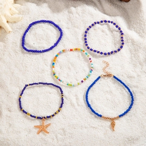 Detail view of 5-piece Bohemian beaded anklet set with starfish and feather charms on sand