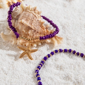 Detail of purple beaded anklets with golden starfish charm on white beach sand