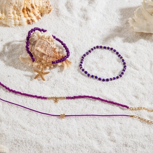 Detail of bohemian purple beaded anklet set with starfish pendant on white beach sand