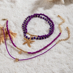 Detail of bohemian purple beaded anklet set with starfish and heart charms on white sand