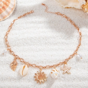 Close-up of bohemian starfish and shell charms on rose gold necklace against beach sand