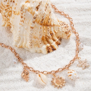 Detail of seashell and starfish pendants on a gold chain necklace over beach sand