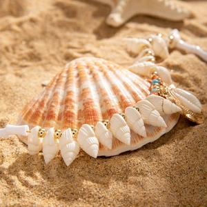 Detail of seashell necklace with gold beads on sand, bohemian beach style jewelry
