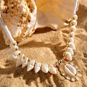 Detail of bohemian shell necklace with golden starfish pendant on sandy beach