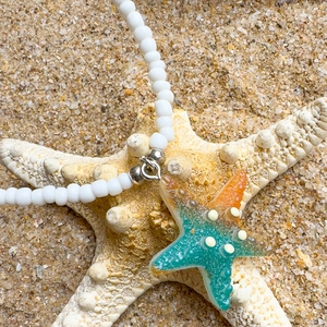 Close-up of bohemian starfish pendant with white beads on a tropical sandy beach