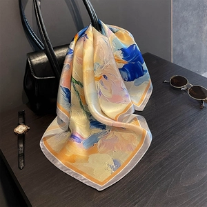Close-up of floral silk scarf with oil painting patterns draped over a black leather handbag